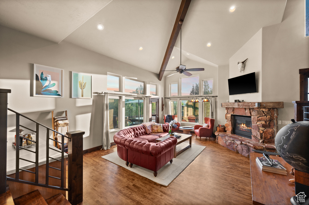 Living room featuring wood finished floors, beam ceiling, a fireplace, high vaulted ceiling, and stairway