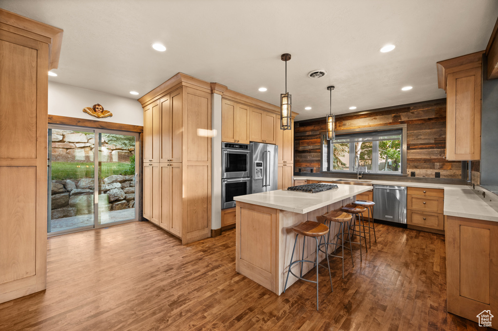 Kitchen with appliances with stainless steel finishes, recessed lighting, light brown cabinetry, a breakfast bar, and a center island