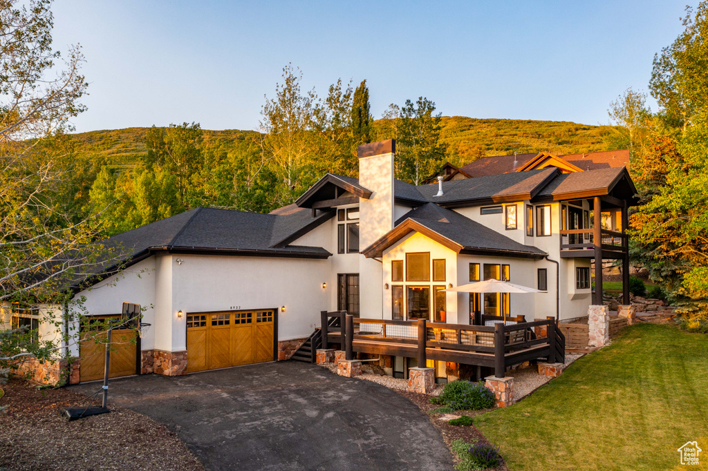 View of front facade featuring a chimney, a garage, driveway, a front lawn, and stone siding