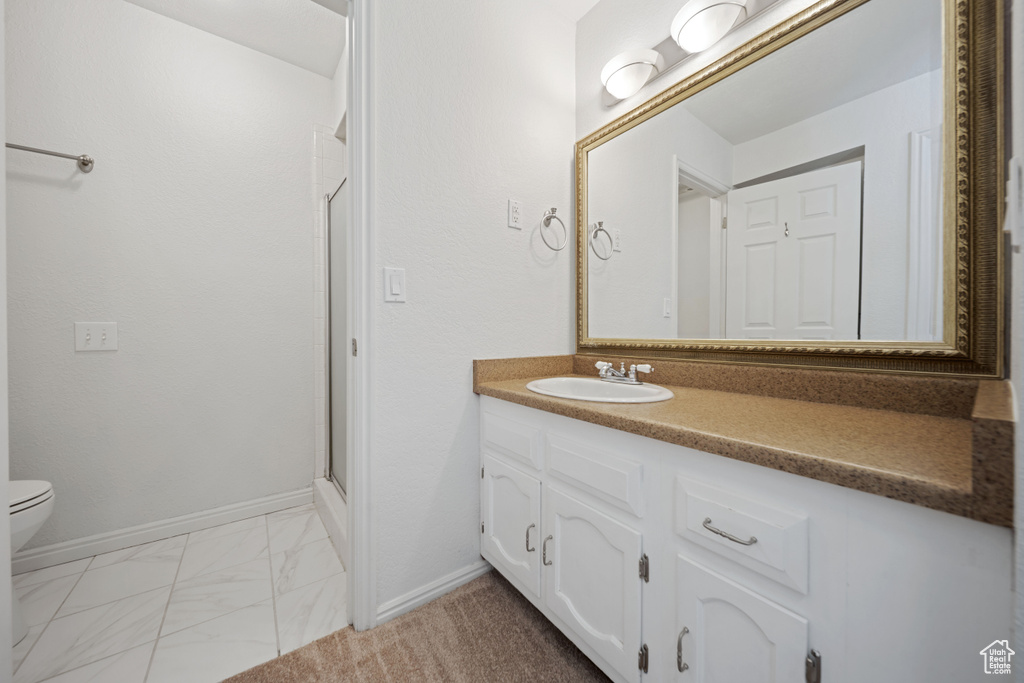 Bathroom featuring vanity, a stall shower, toilet, marble look tiles, and baseboards