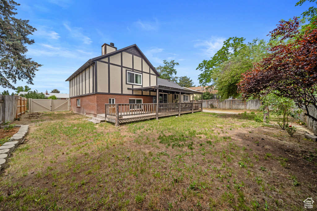 Back of property with a chimney, brick siding, a deck, and a gate