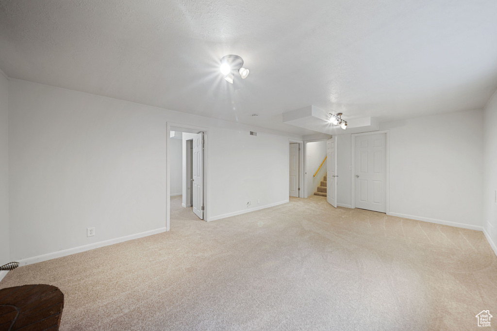Unfurnished living room featuring light colored carpet, baseboards, and stairs