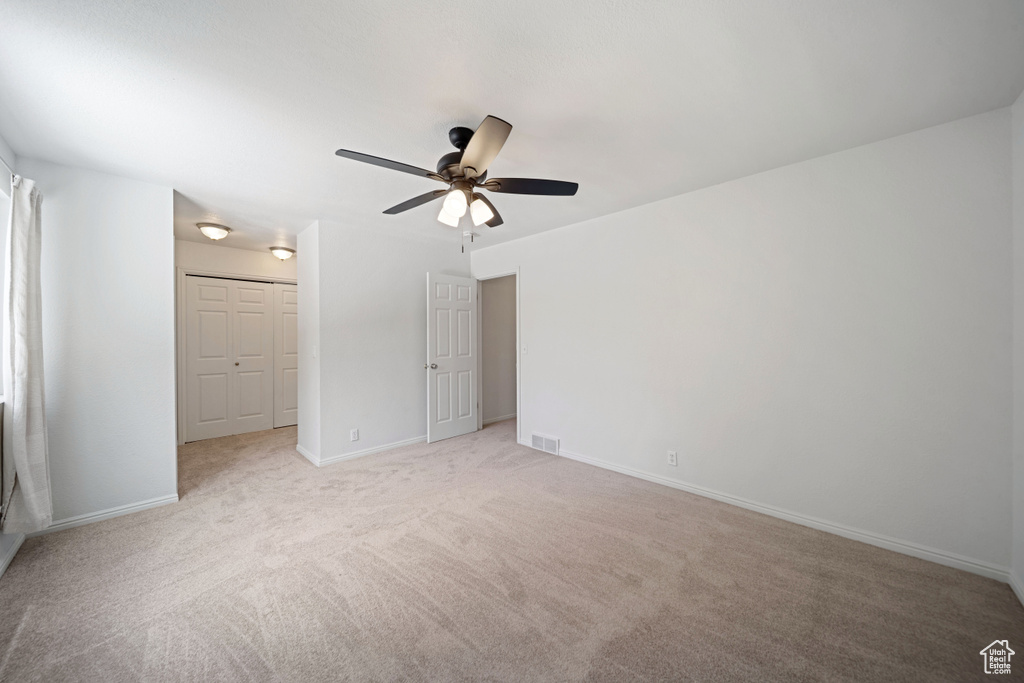 Unfurnished bedroom with light colored carpet, baseboards, and a ceiling fan