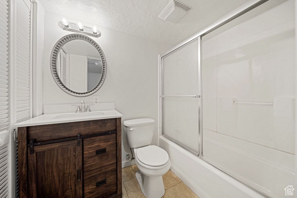 Bathroom featuring vanity, toilet, tile patterned flooring, enclosed tub / shower combo, and a textured ceiling