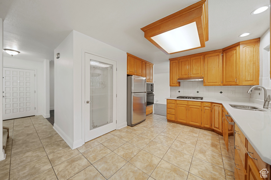 Kitchen with stainless steel appliances, a sink, under cabinet range hood, light countertops, and light tile patterned floors