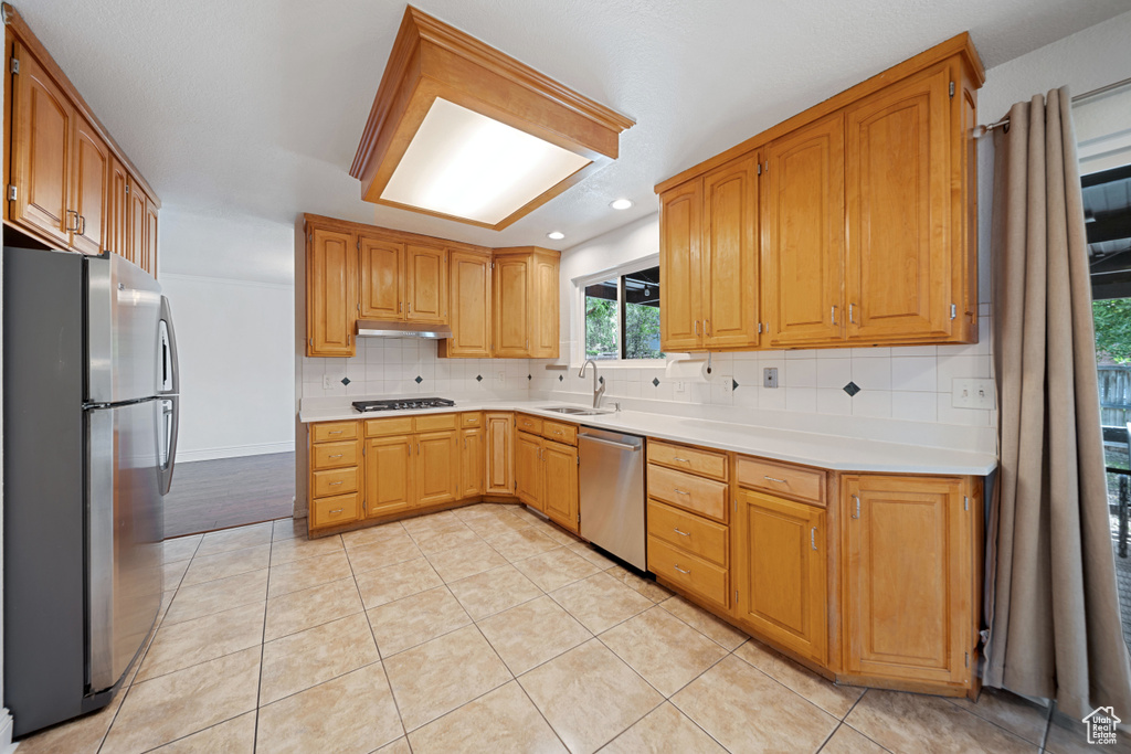 Kitchen featuring appliances with stainless steel finishes, a sink, under cabinet range hood, backsplash, and light countertops