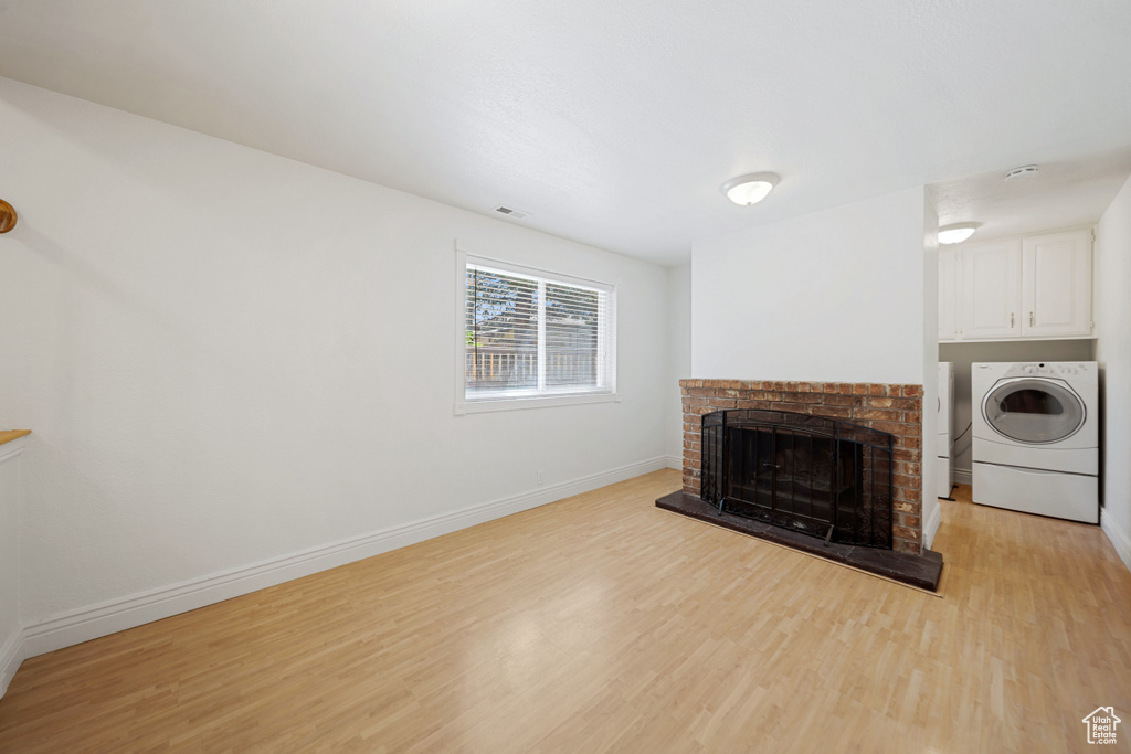 Unfurnished living room featuring light wood-type flooring, a brick fireplace, baseboards, and separate washer and dryer