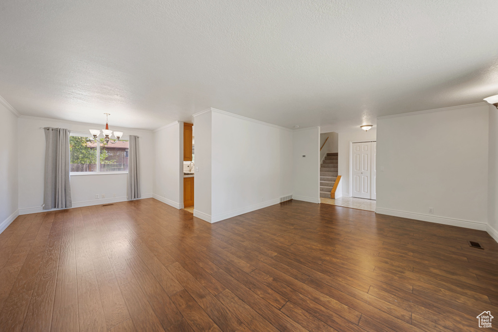 Unfurnished living room featuring a chandelier, stairs, dark wood-type flooring, baseboards, and a textured ceiling