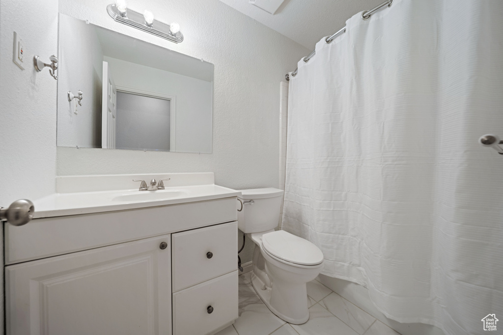 Bathroom with toilet, vanity, marble finish floors, and curtained shower
