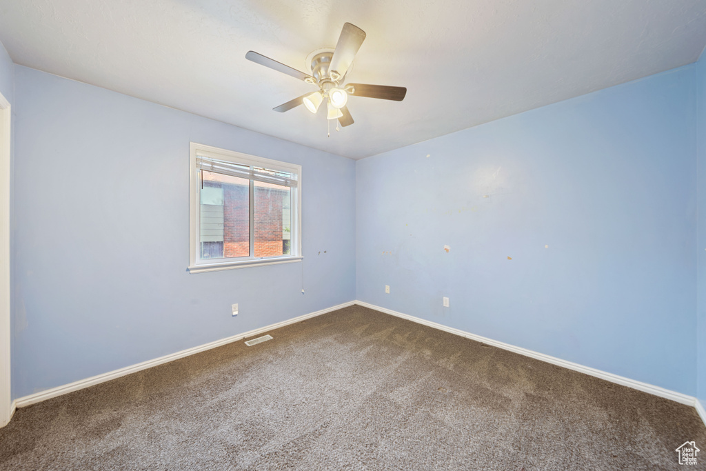 Empty room with dark colored carpet, ceiling fan, and baseboards