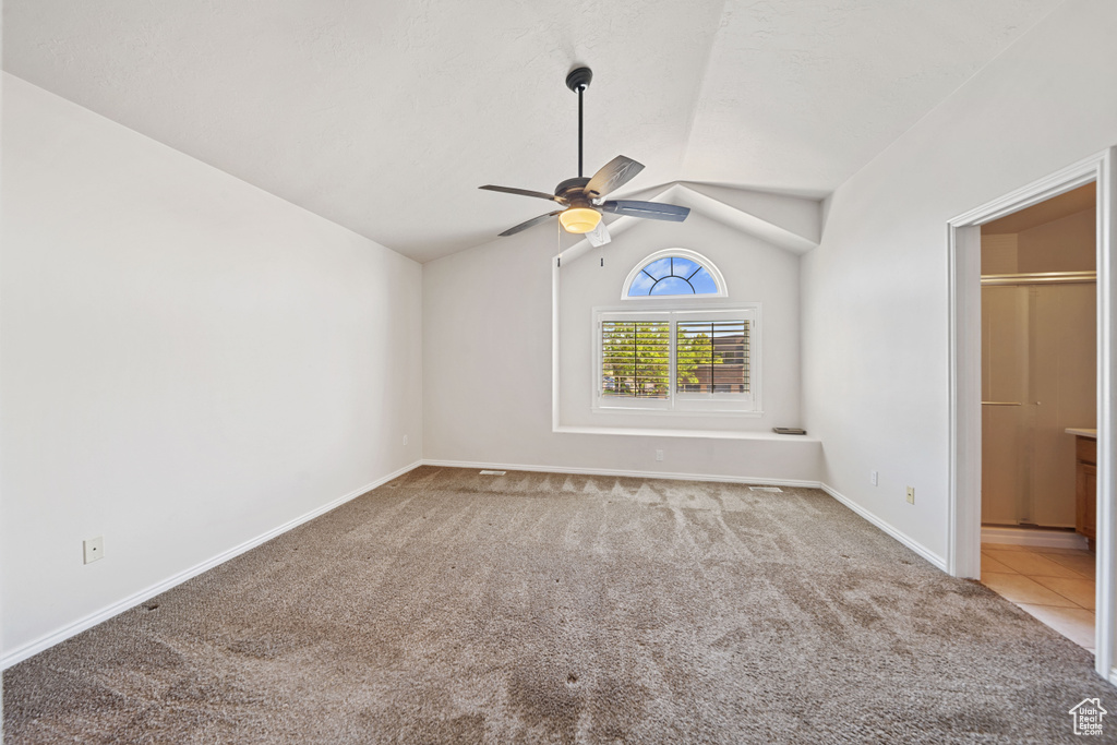 Empty room featuring carpet flooring, ceiling fan, baseboards, and vaulted ceiling