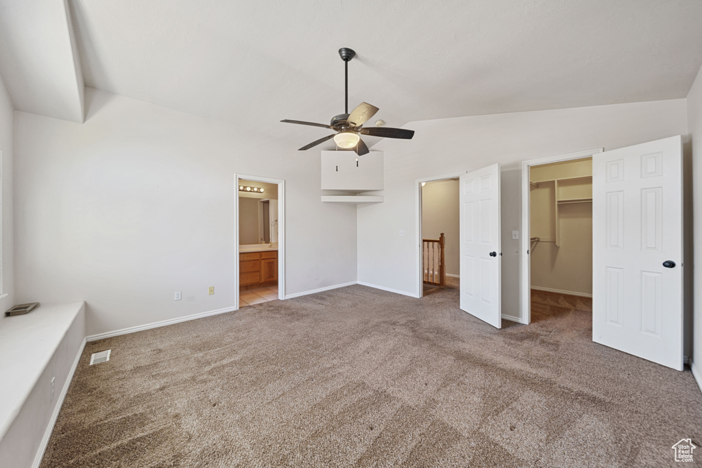 Unfurnished bedroom featuring lofted ceiling, a spacious closet, carpet, baseboards, and connected bathroom