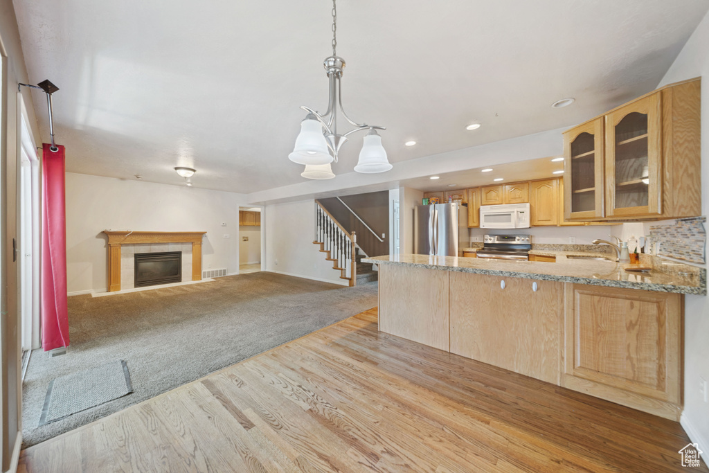 Kitchen with stainless steel appliances, light wood-style floors, light stone counters, glass insert cabinets, and light brown cabinets