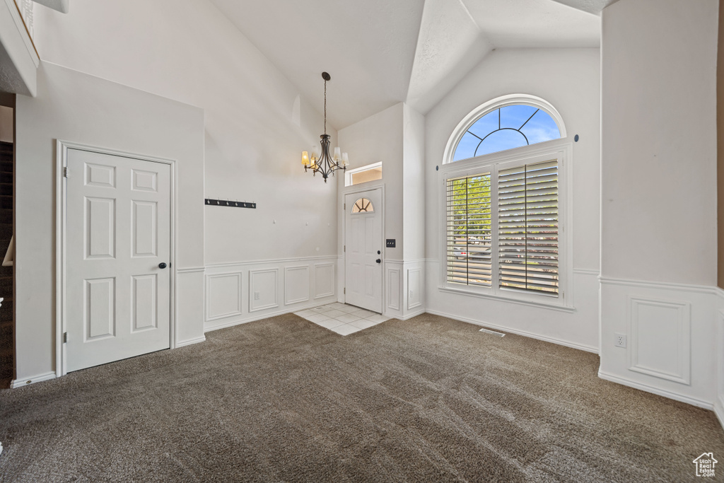 Foyer with carpet, a chandelier, a wainscoted wall, high vaulted ceiling, and a decorative wall