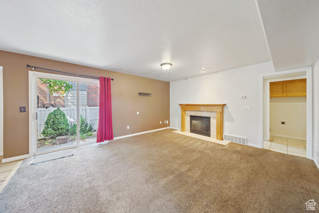 Unfurnished living room featuring baseboards, a tile fireplace, and light carpet