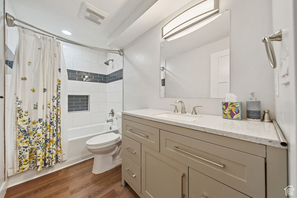 Bathroom featuring vanity, toilet, wood finished floors, shower / bathtub combination with curtain, and recessed lighting