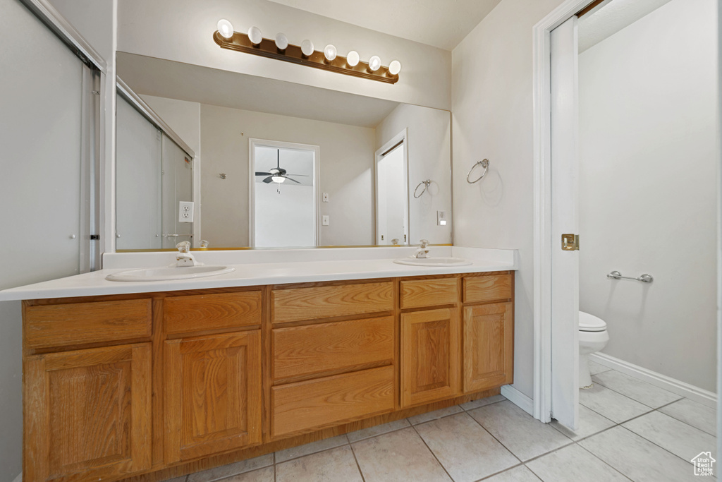 Full bathroom with double vanity, tile patterned floors, toilet, and ceiling fan
