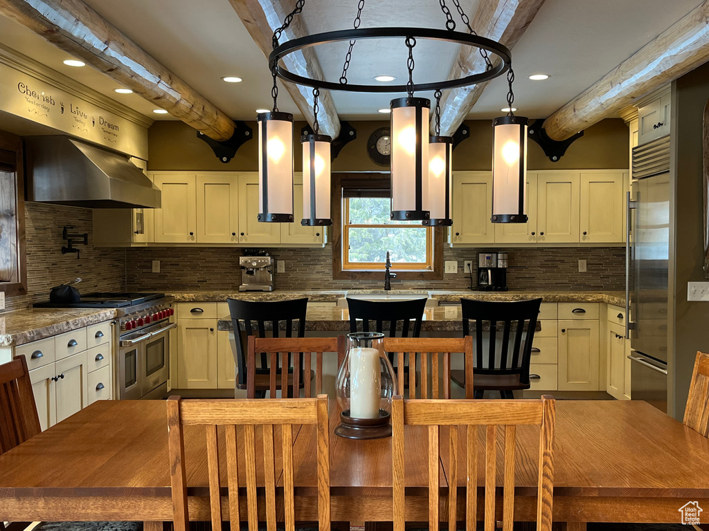 Kitchen featuring high end appliances, beam ceiling, wall chimney range hood, decorative backsplash, and a sink