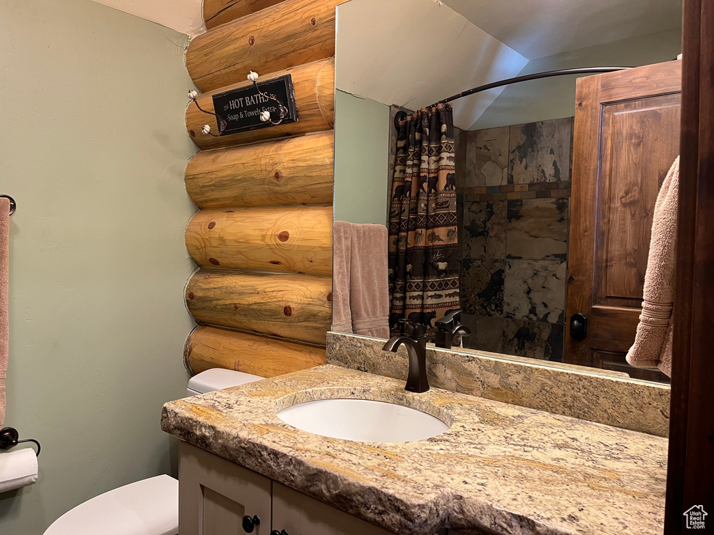 Bathroom featuring toilet, vanity, curtained shower, and log walls