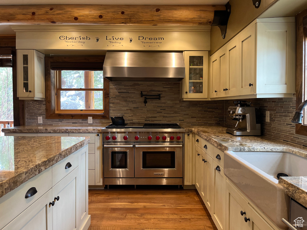 Kitchen with range with two ovens, wall chimney range hood, a sink, wood finished floors, and tasteful backsplash