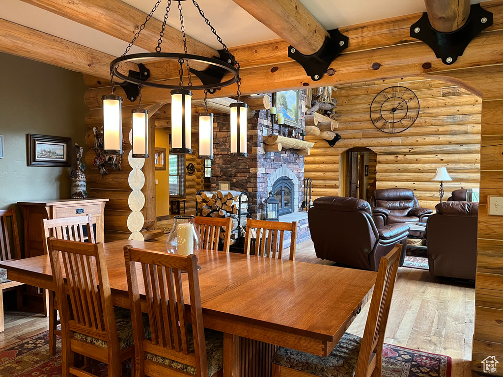 Dining space featuring rustic walls, wood-type flooring, beamed ceiling, and a stone fireplace