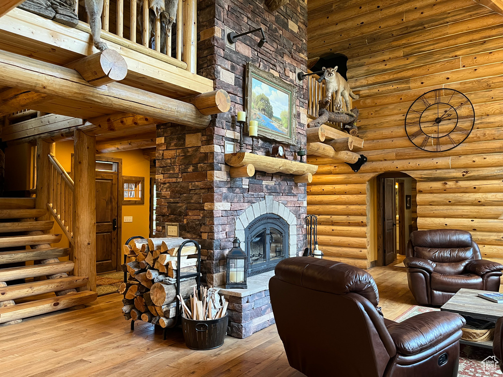 Living room featuring hardwood / wood-style flooring, a stone fireplace, stairway, a towering ceiling, and rustic walls