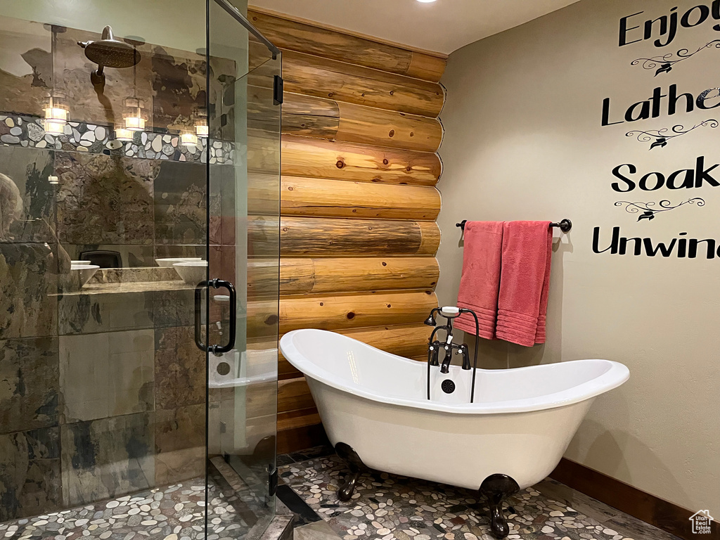 Full bathroom with rustic walls, a stall shower, a freestanding bath, and baseboards