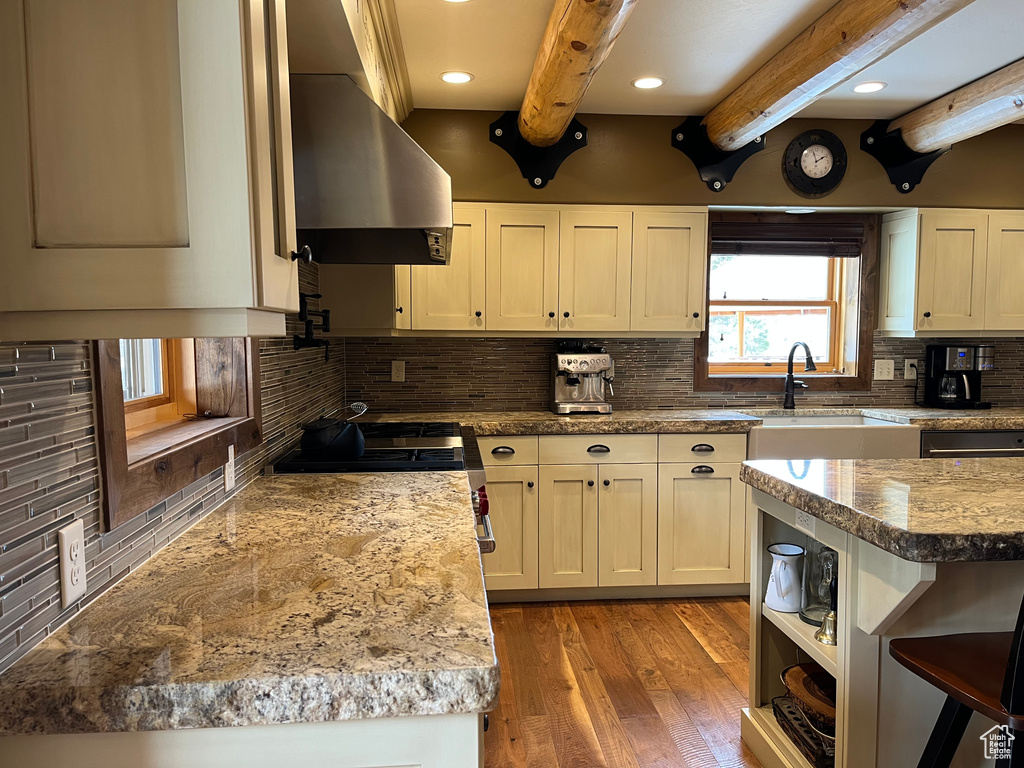 Kitchen featuring wall chimney exhaust hood, beam ceiling, tasteful backsplash, light wood finished floors, and a sink
