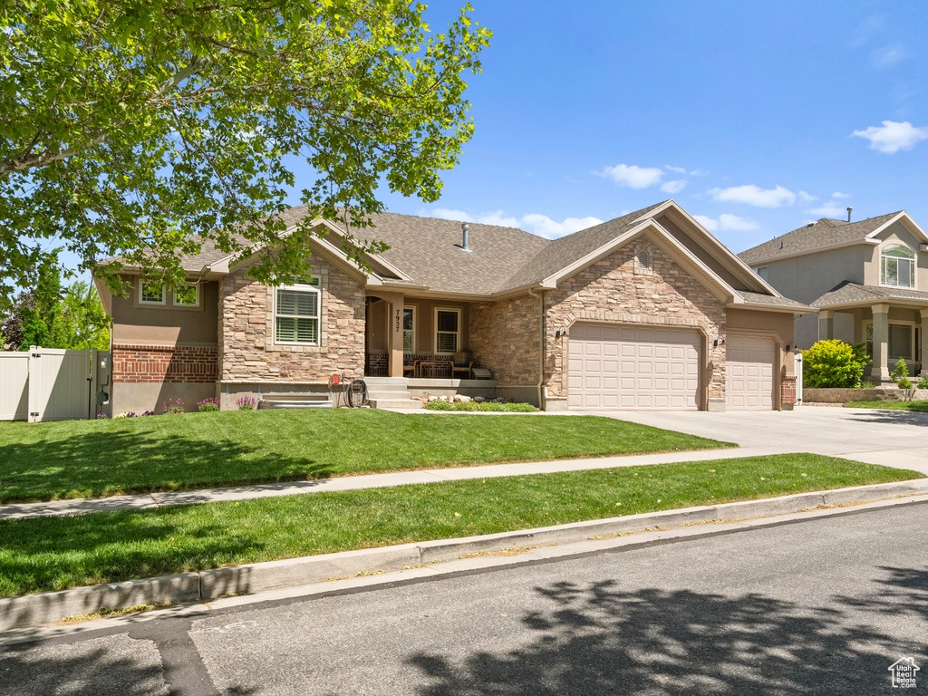 View of front facade featuring stone siding, an attached garage, a gate, driveway, and a shingled roof