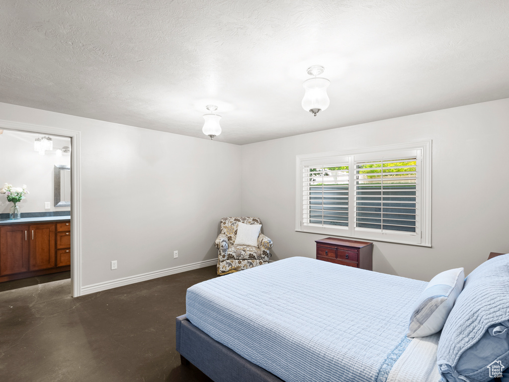 Bedroom with baseboards, ensuite bath, and finished concrete flooring