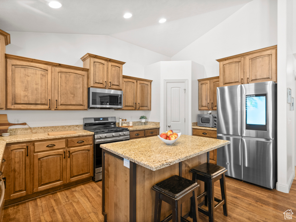 Kitchen with appliances with stainless steel finishes, a kitchen island, a kitchen breakfast bar, light stone countertops, and wood finished floors
