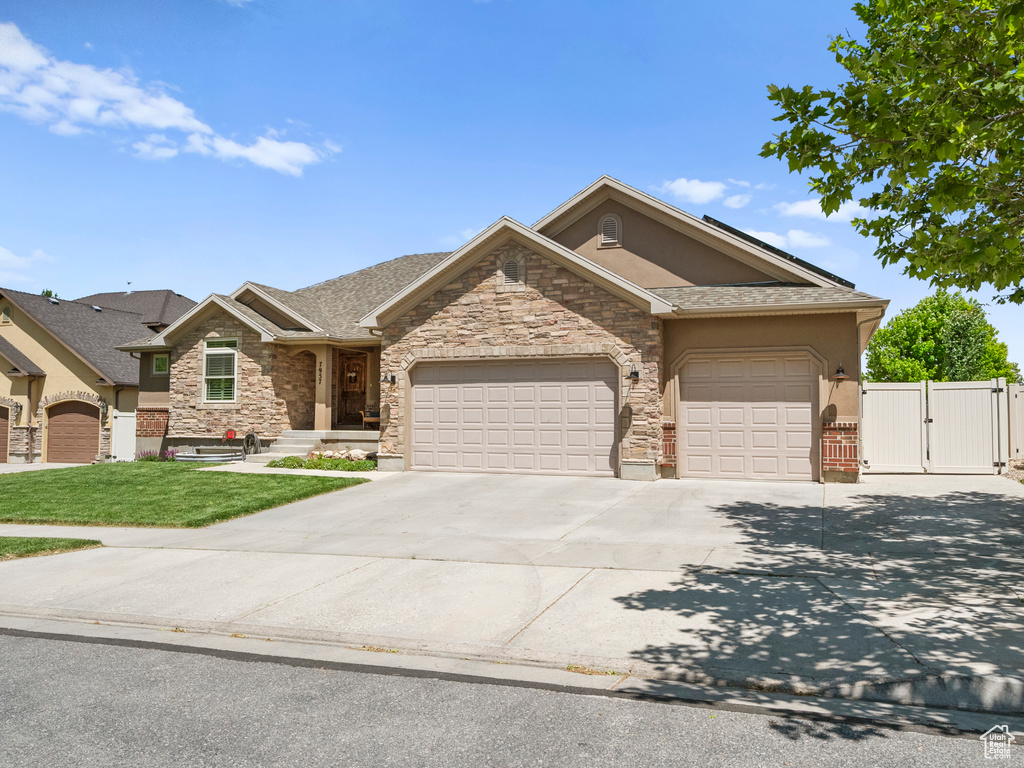 View of front of property featuring a gate, a garage, concrete driveway, stone siding, and stucco siding
