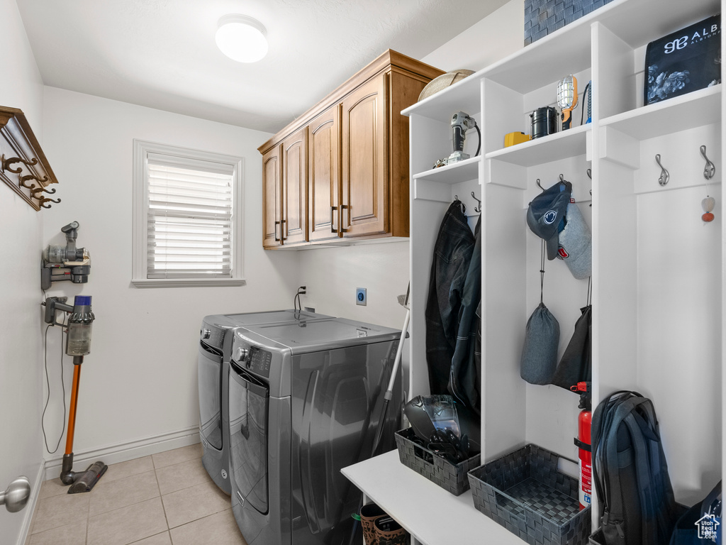Laundry room featuring washing machine and dryer, light tile patterned floors, cabinet space, and baseboards