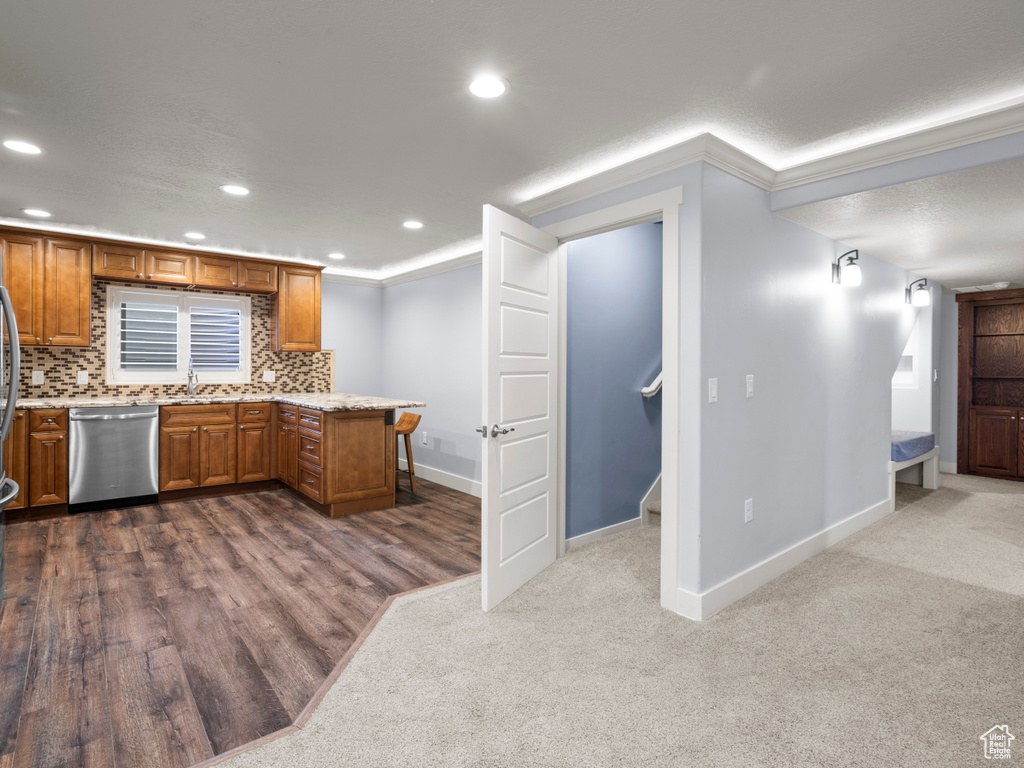 Kitchen featuring stainless steel dishwasher, brown cabinetry, baseboards, a peninsula, and ornamental molding