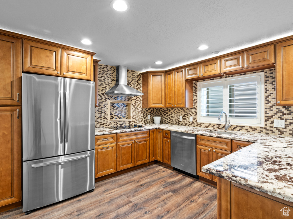 Kitchen with appliances with stainless steel finishes, a sink, wall chimney range hood, brown cabinetry, and recessed lighting