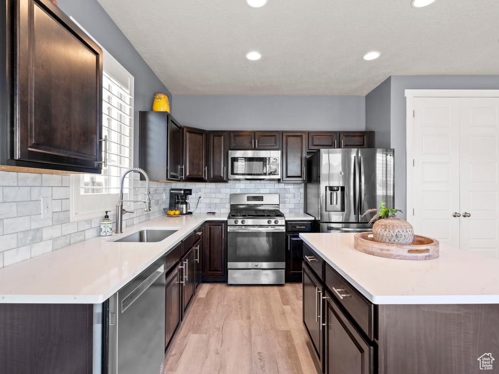 Kitchen with stainless steel appliances, a sink, dark brown cabinetry, light wood-style flooring, and a kitchen island