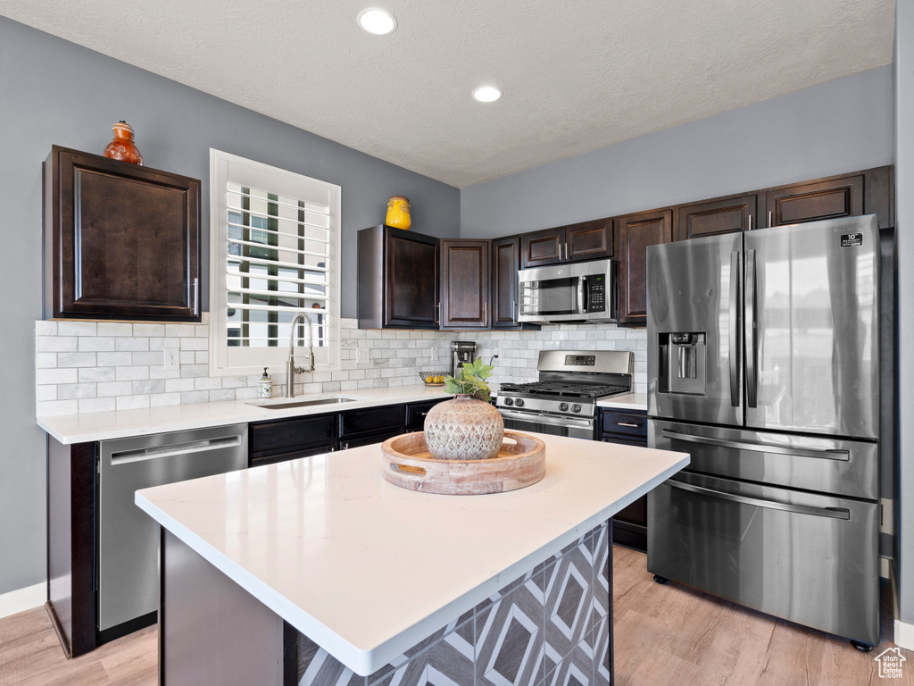 Kitchen with stainless steel appliances, a sink, dark brown cabinets, light countertops, and recessed lighting