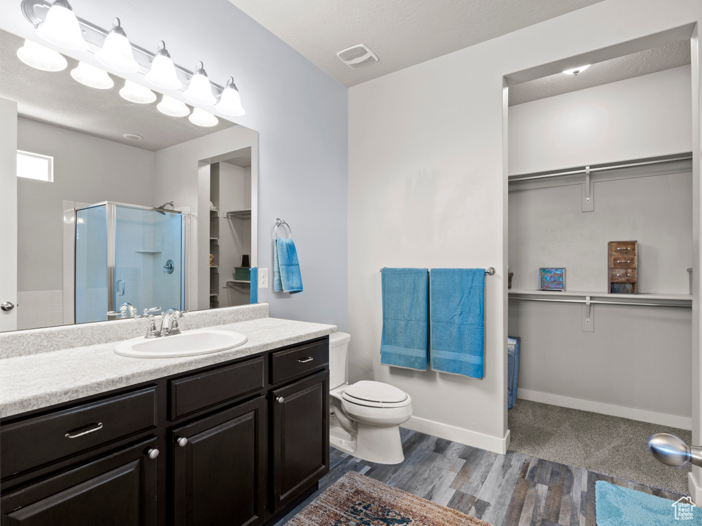 Full bath with a walk in closet, a stall shower, vanity, wood finished floors, and toilet