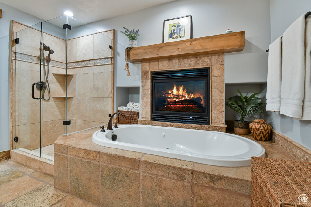 Bathroom with stone tile floors, a tub with jets, a stall shower, and a tile fireplace
