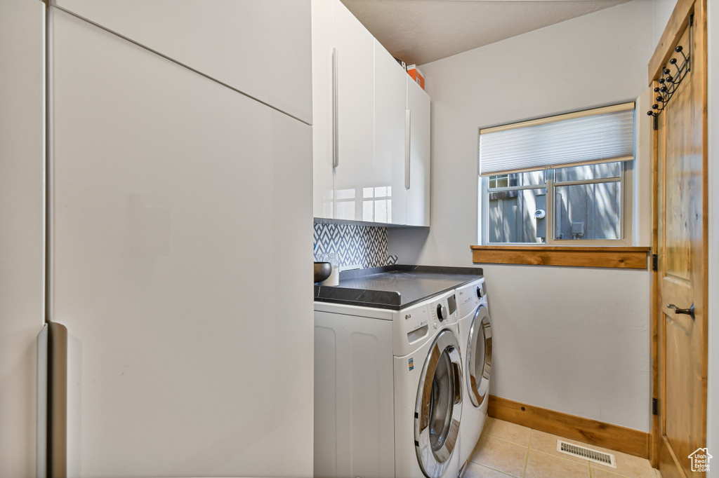 Washroom with cabinet space, independent washer and dryer, light tile patterned flooring, and baseboards
