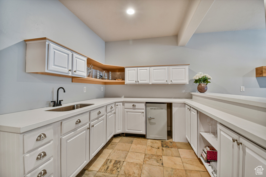 Kitchen with a sink, open shelves, light stone finish floors, and white cabinetry