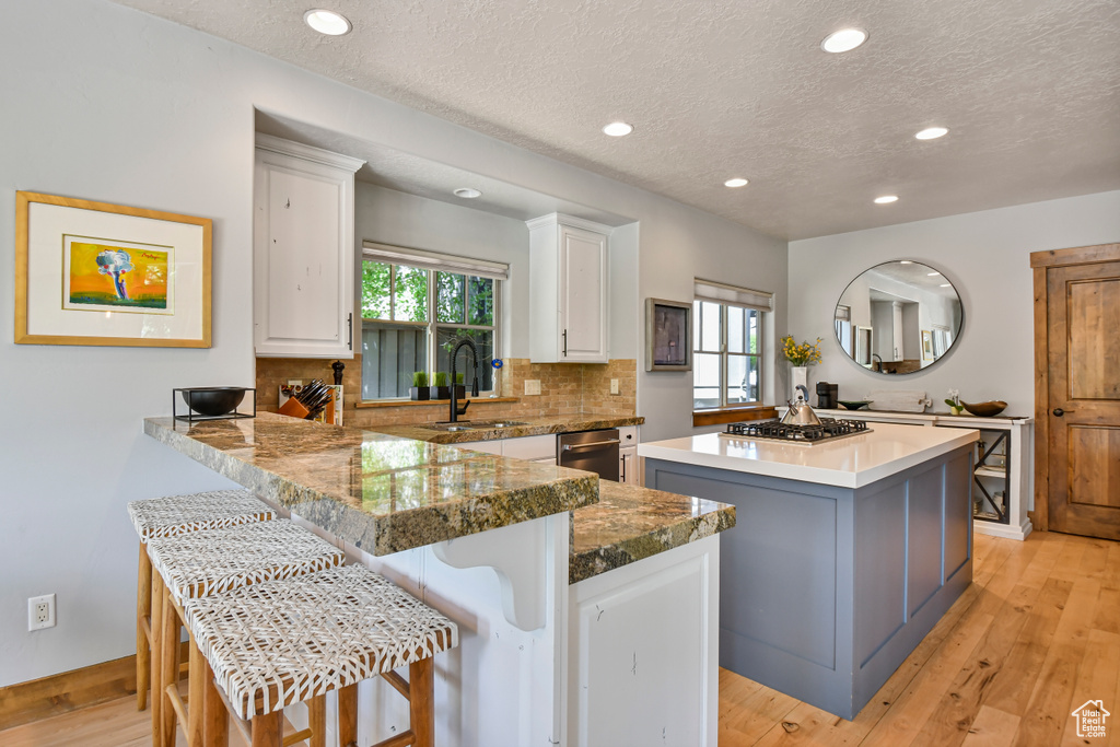 Kitchen featuring a center island, a textured ceiling, white cabinets, a sink, and backsplash