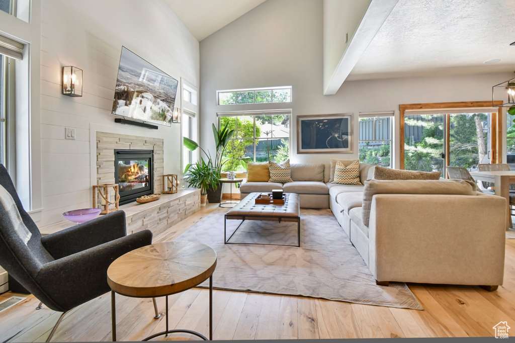 Living room featuring high vaulted ceiling, light wood finished floors, and a stone fireplace