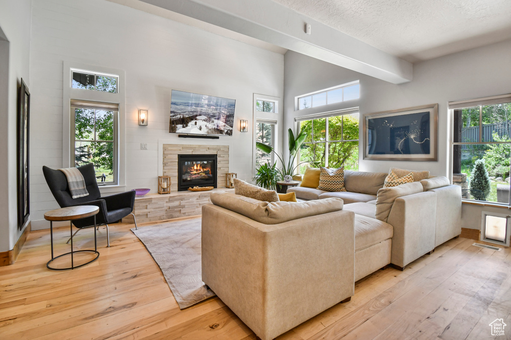 Living room with light wood-style floors, a stone fireplace, a textured ceiling, and a high ceiling