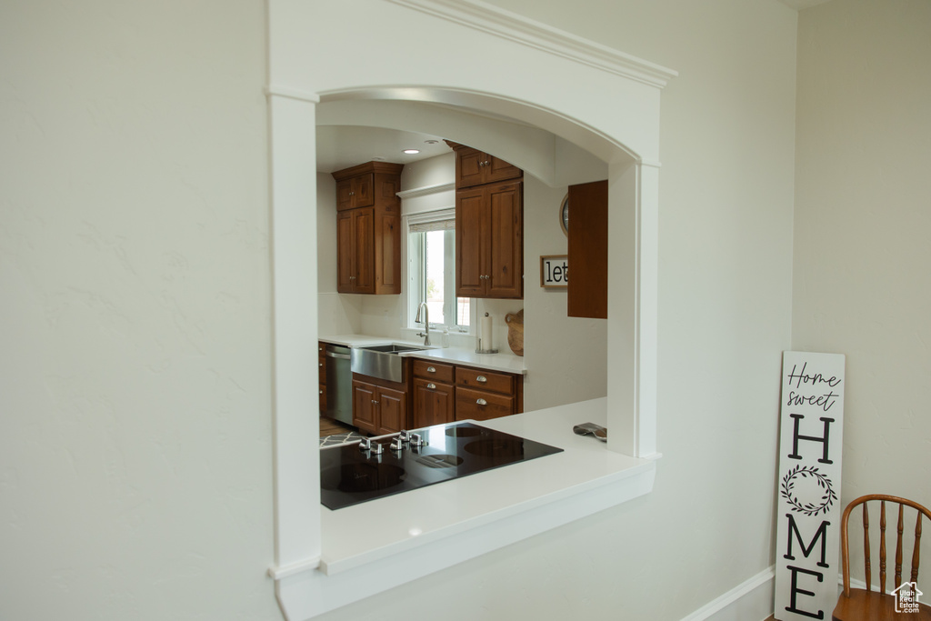 Kitchen with a sink, black electric cooktop, stainless steel dishwasher, arched walkways, and light countertops