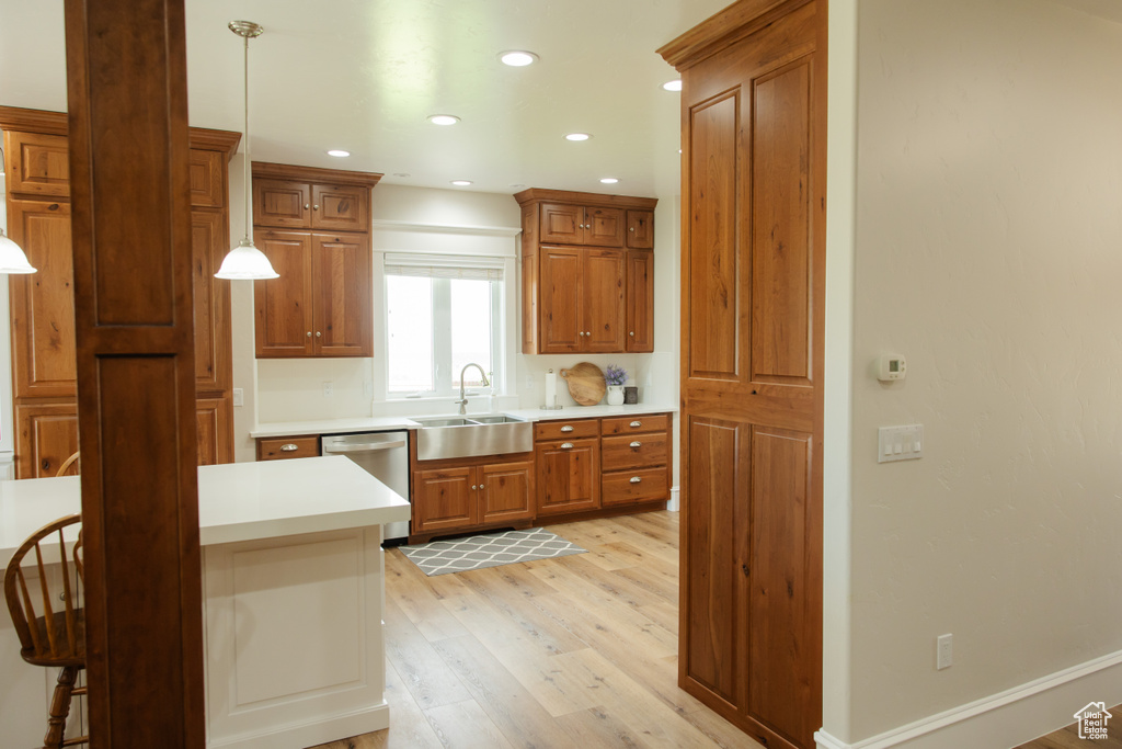 Kitchen featuring stainless steel dishwasher, a sink, light wood-type flooring, brown cabinetry, and light countertops