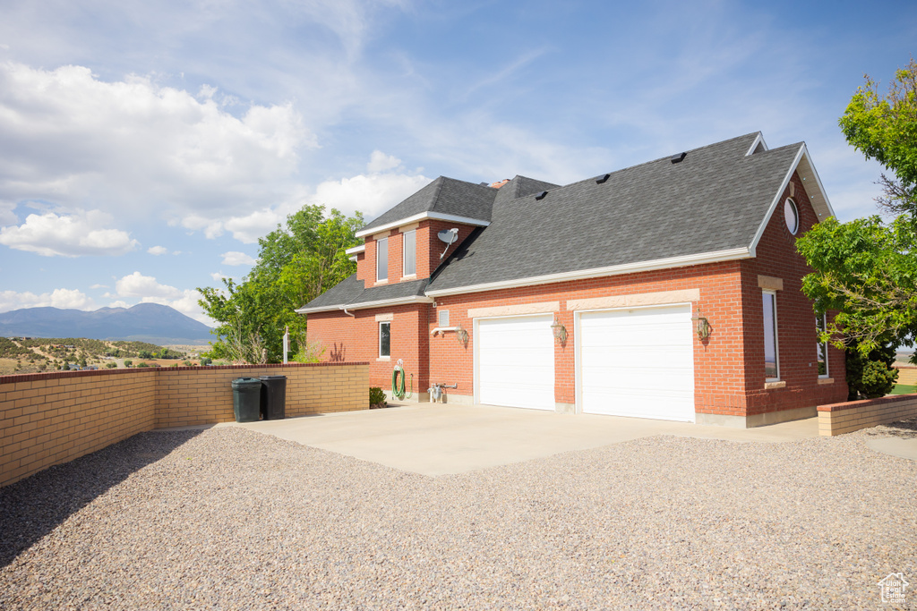 View of side of home featuring a shingled roof, driveway, and brick siding