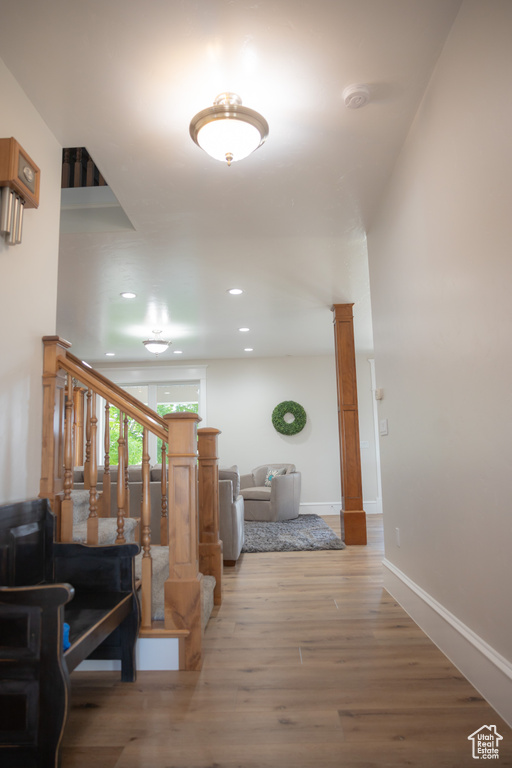 Corridor with ornate columns, light wood-style flooring, stairs, baseboards, and recessed lighting