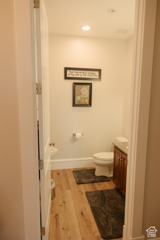 Half bath with wood finished floors, toilet, vanity, baseboards, and recessed lighting