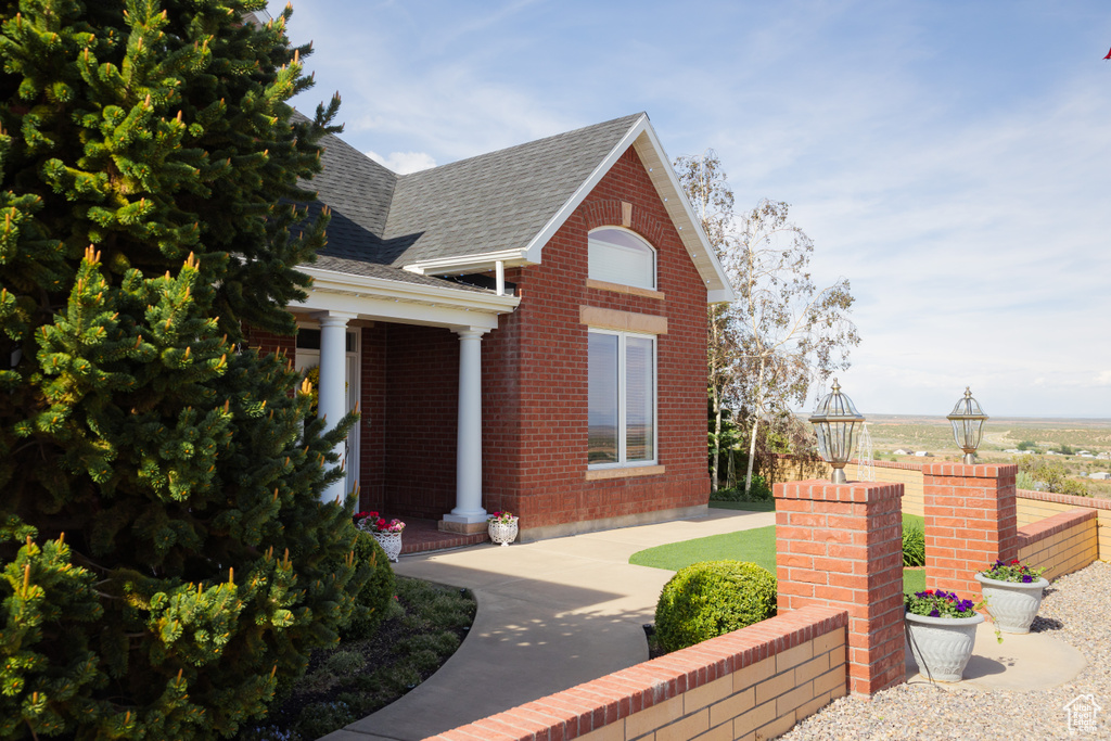View of front of property with a shingled roof, brick siding, and covered porch